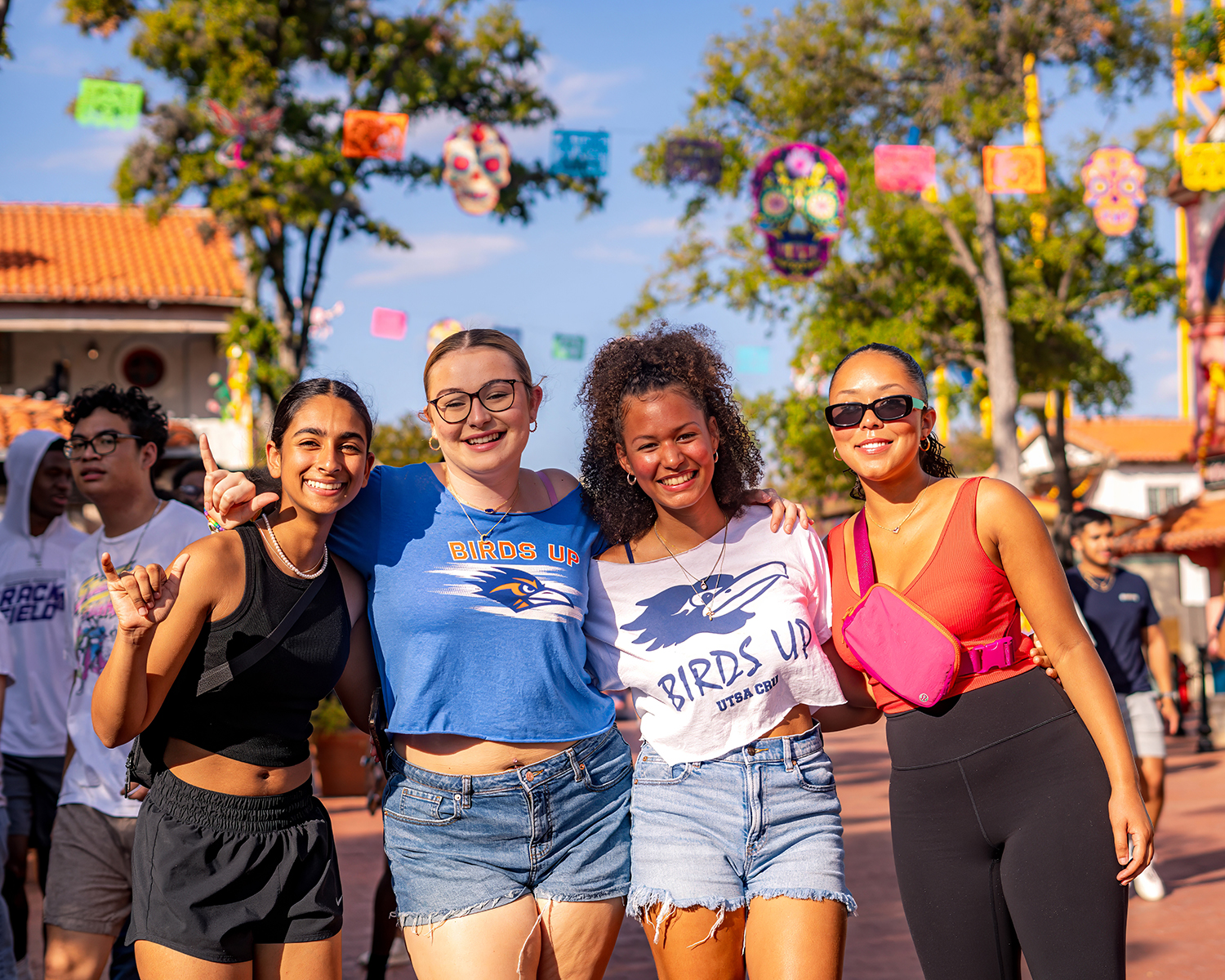 From left to right, A group of women posing in front of Six Flags, smiling and holding up the schools "birds up" hand gesture.